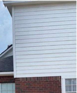 The side of a brick house with white siding and a window.