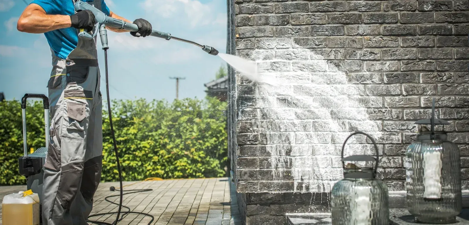 A man is cleaning a brick wall with a high pressure washer.