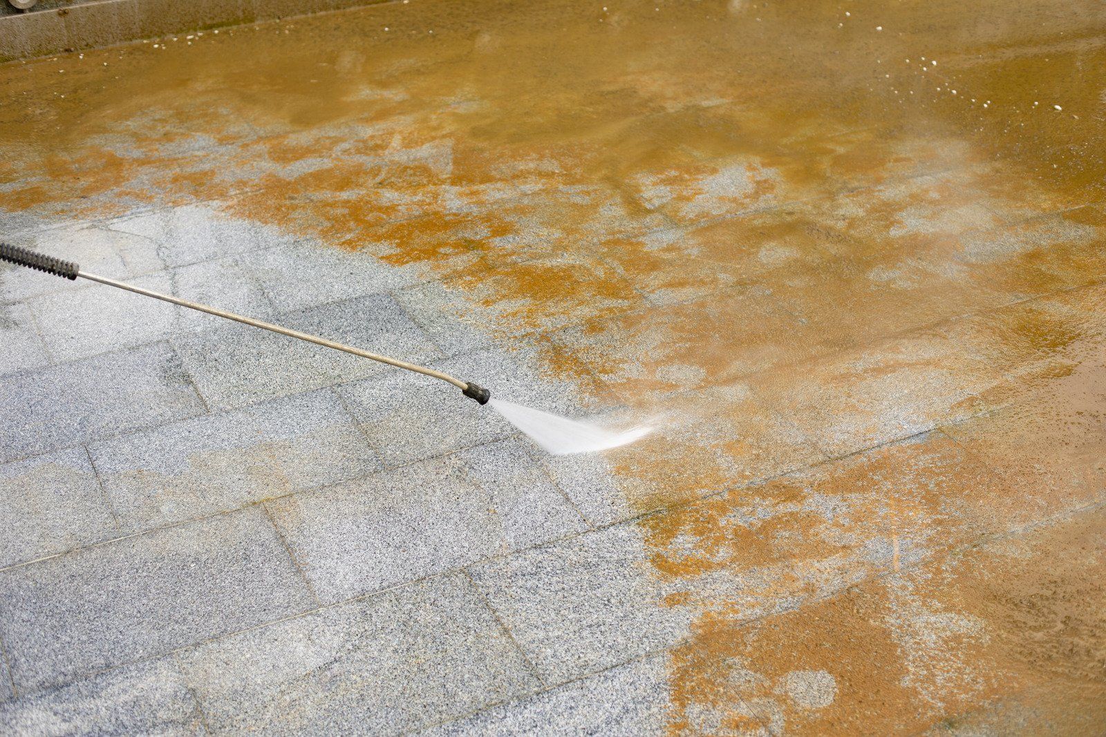 A person is using a high pressure washer to clean a brick walkway.