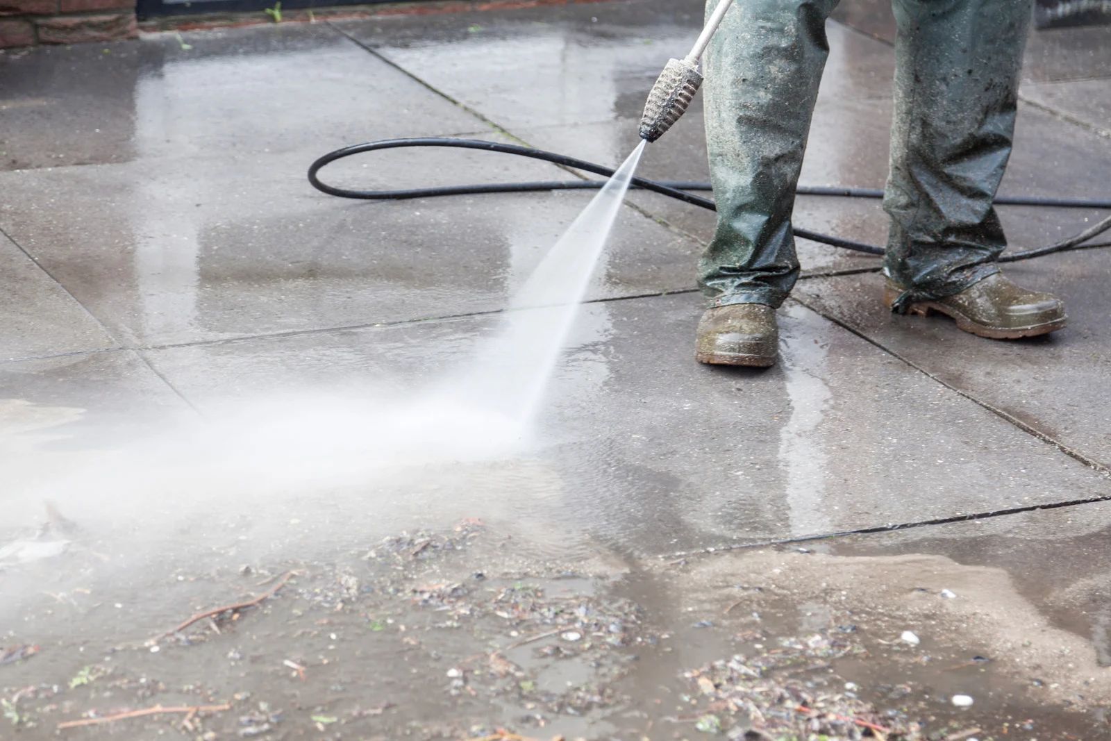 Person power washing a stone patio, water spraying, wet ground.