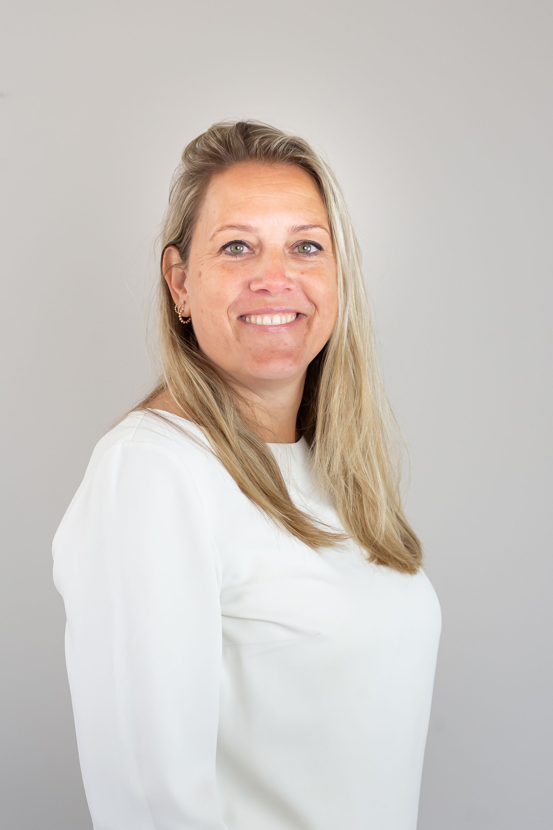 Een vrouw zit aan een tafel, haar handen gevouwen en glimlachend.