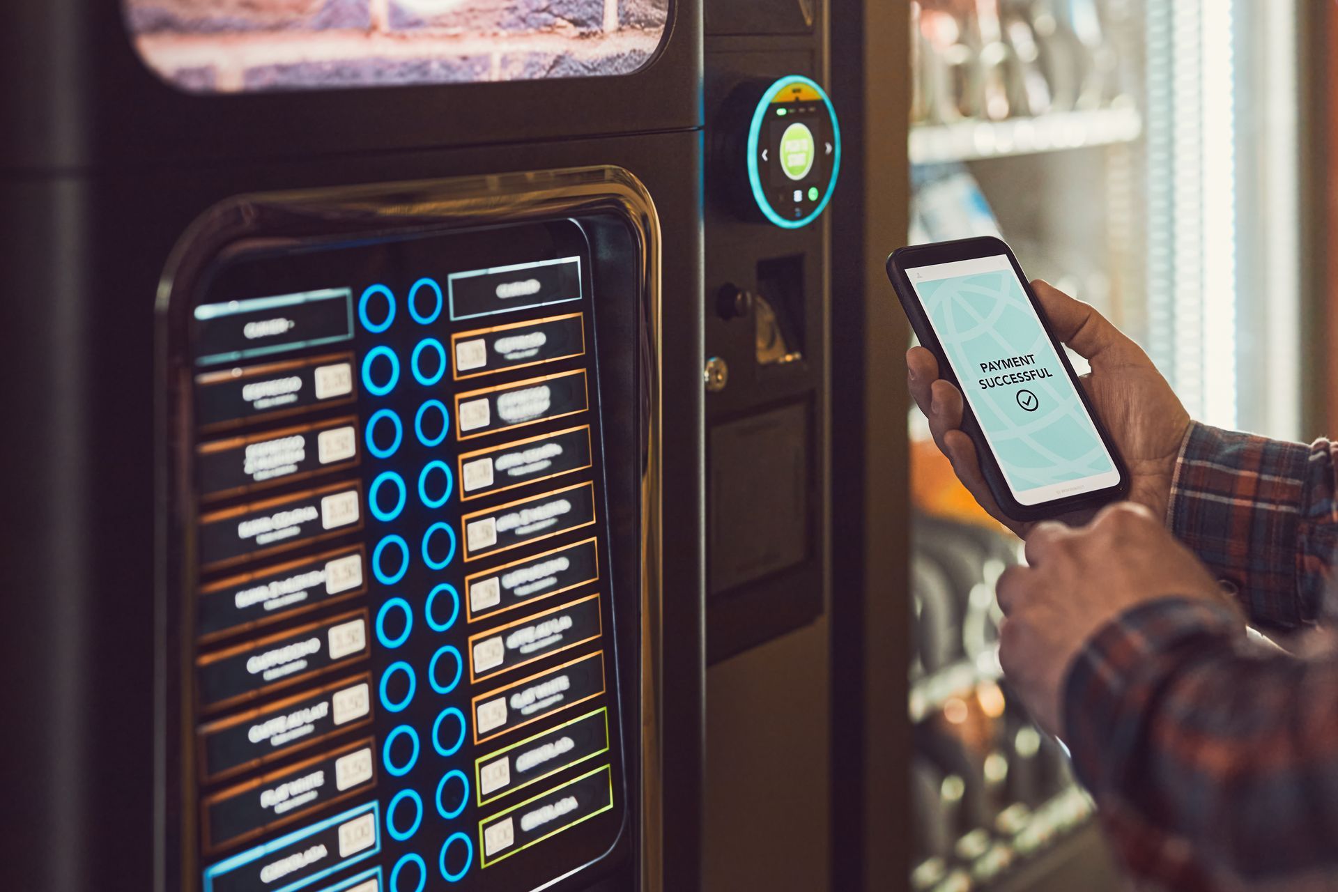 A person uses a smartphone to pay for a drink at a modern, digital vending machine.