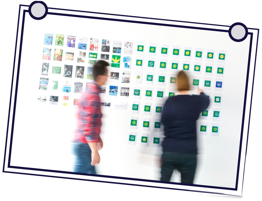 Two people blurred next to a wall covered with sticky notes and small pictures.