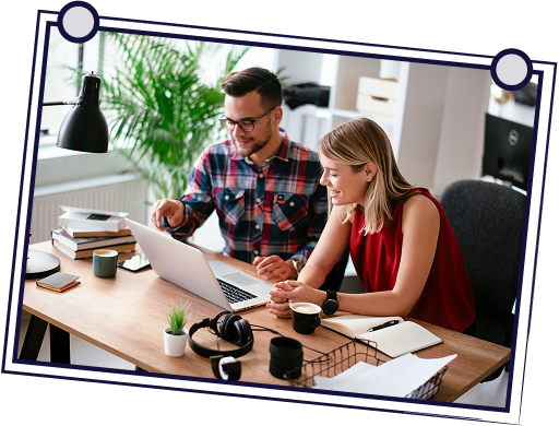 Two people at a desk looking at a laptop. The man points at the screen, and the woman smiles.