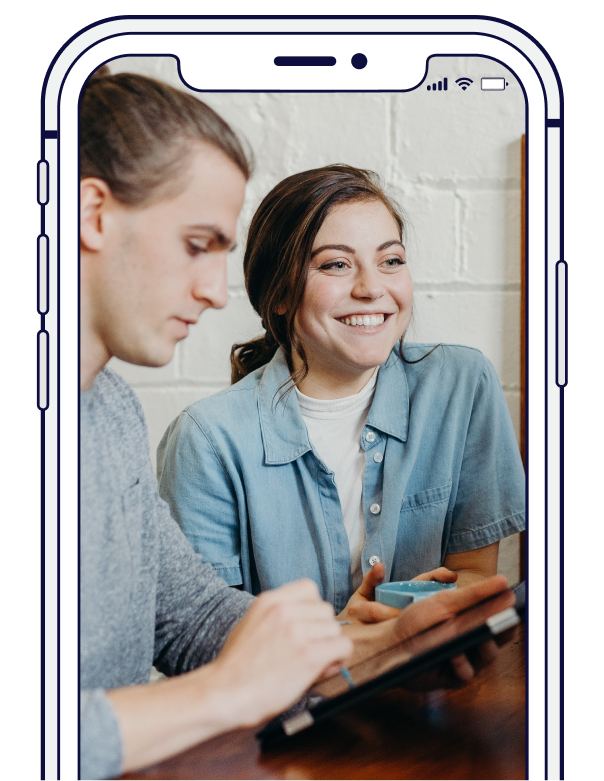 Two people looking at a tablet together, smiling. One points to the screen. Indoors.