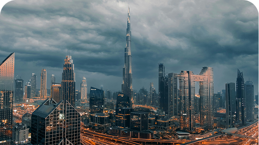 Dubai skyline at dusk, with the Burj Khalifa towering over illuminated skyscrapers under a cloudy sky.