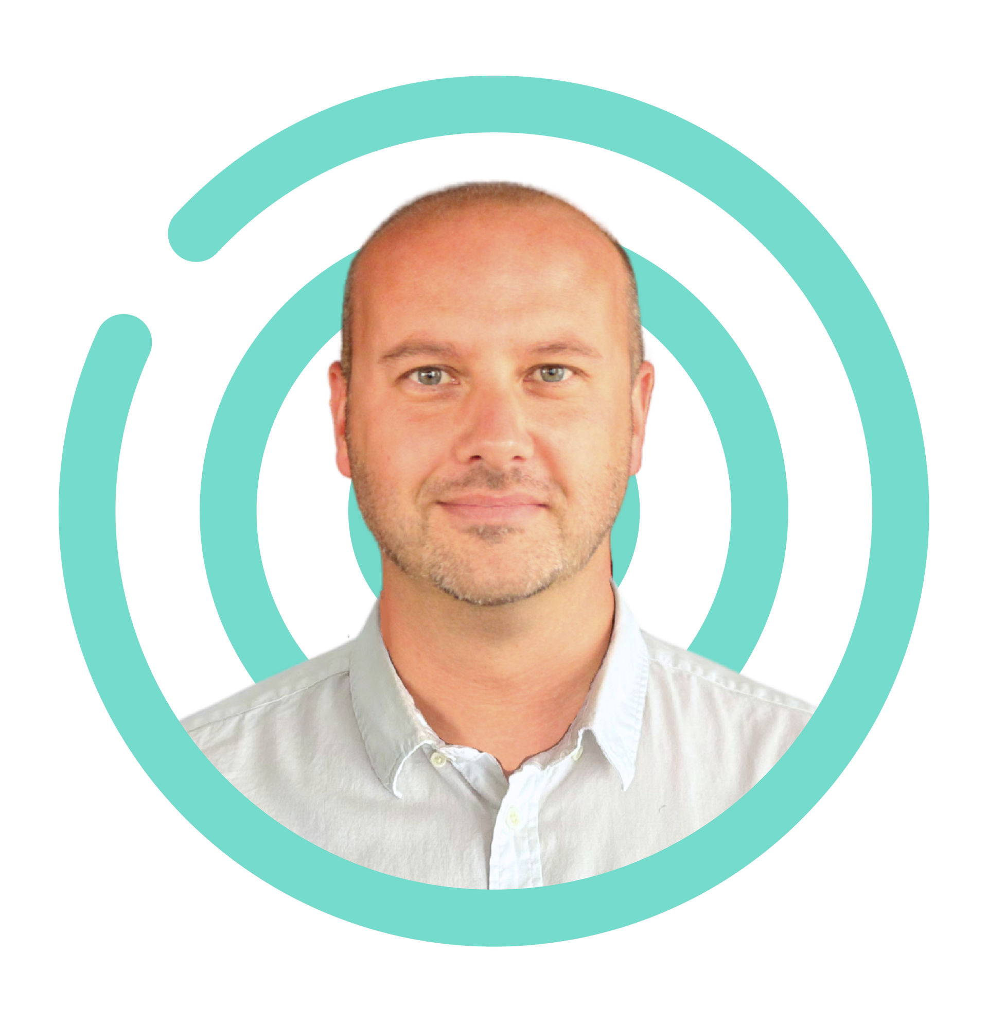 Man with a shaved head smiles, wearing a light blue button-down shirt, set against a dark blue, concentric circle design.