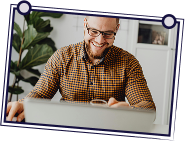 Group of people in a meeting. A man stands, gesturing while holding papers, while others sit around a table.