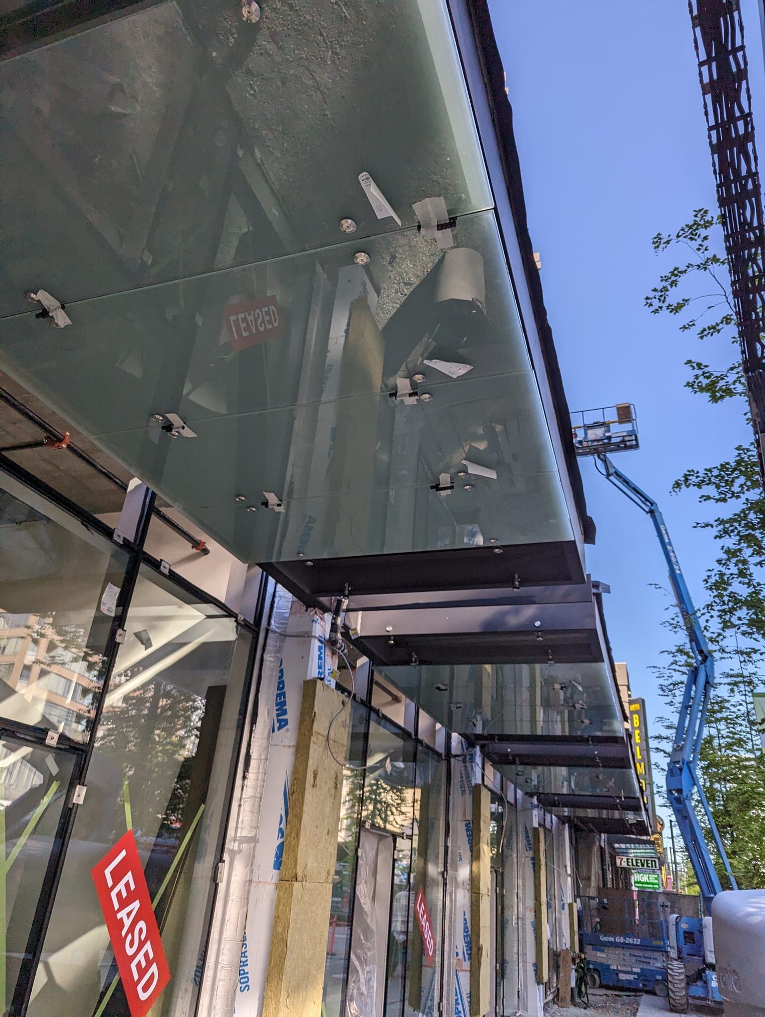 A glass canopy is being installed on the side of a building.