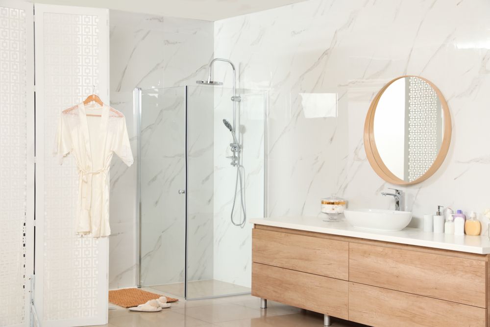 Modern bathroom with marble walls, glass shower, wooden vanity, and circular mirror. — Kincumber Glass & Glazing in Kincumber, NSW