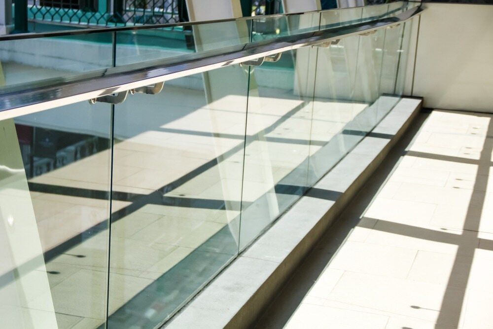 Glass railing with metal top, casting shadows on a light-colored floor. — Kincumber Glass & Glazing in Kincumber, NSW