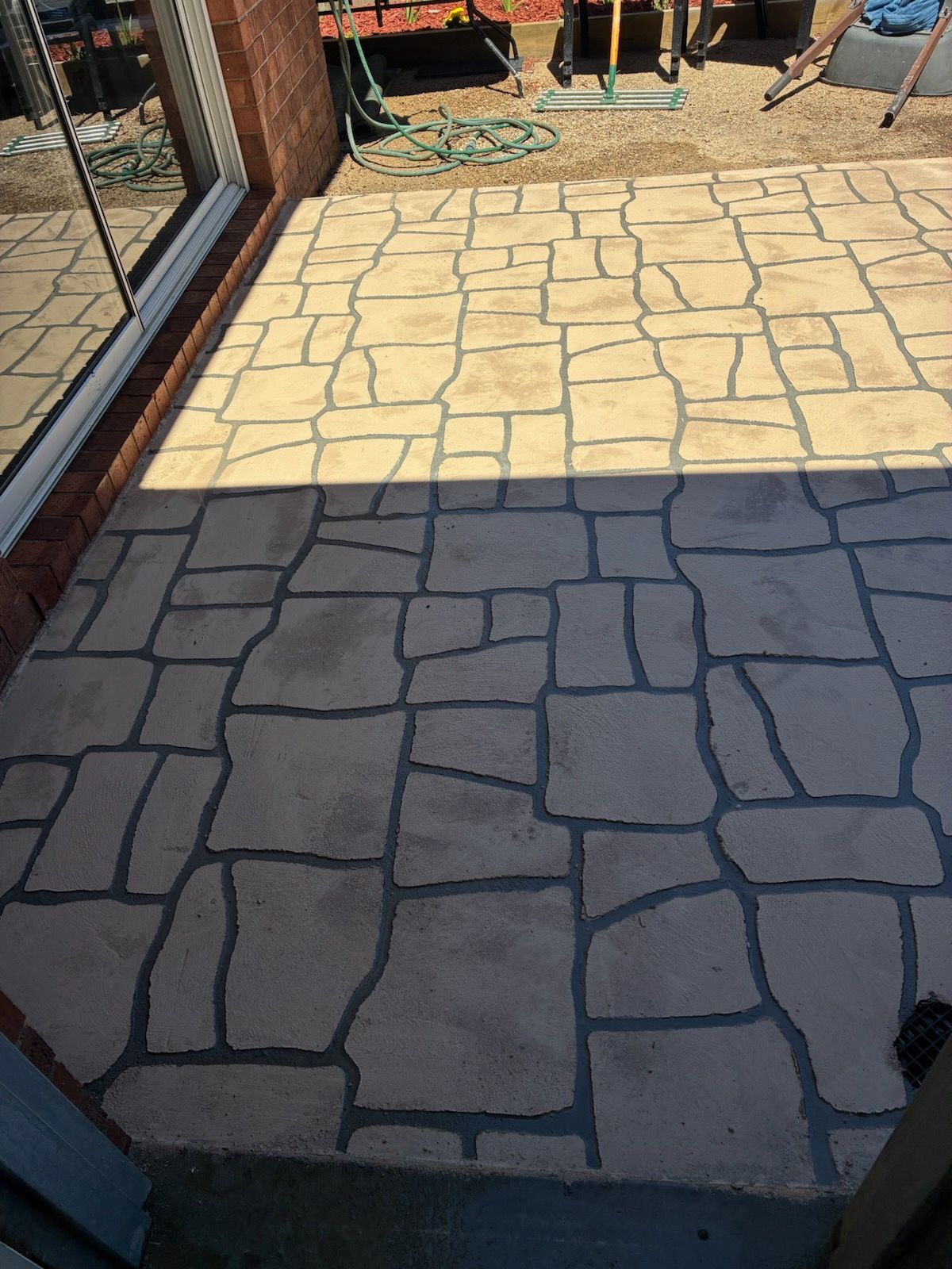Patio with light-colored stone pattern, dark gray grout lines, and partial shadow.