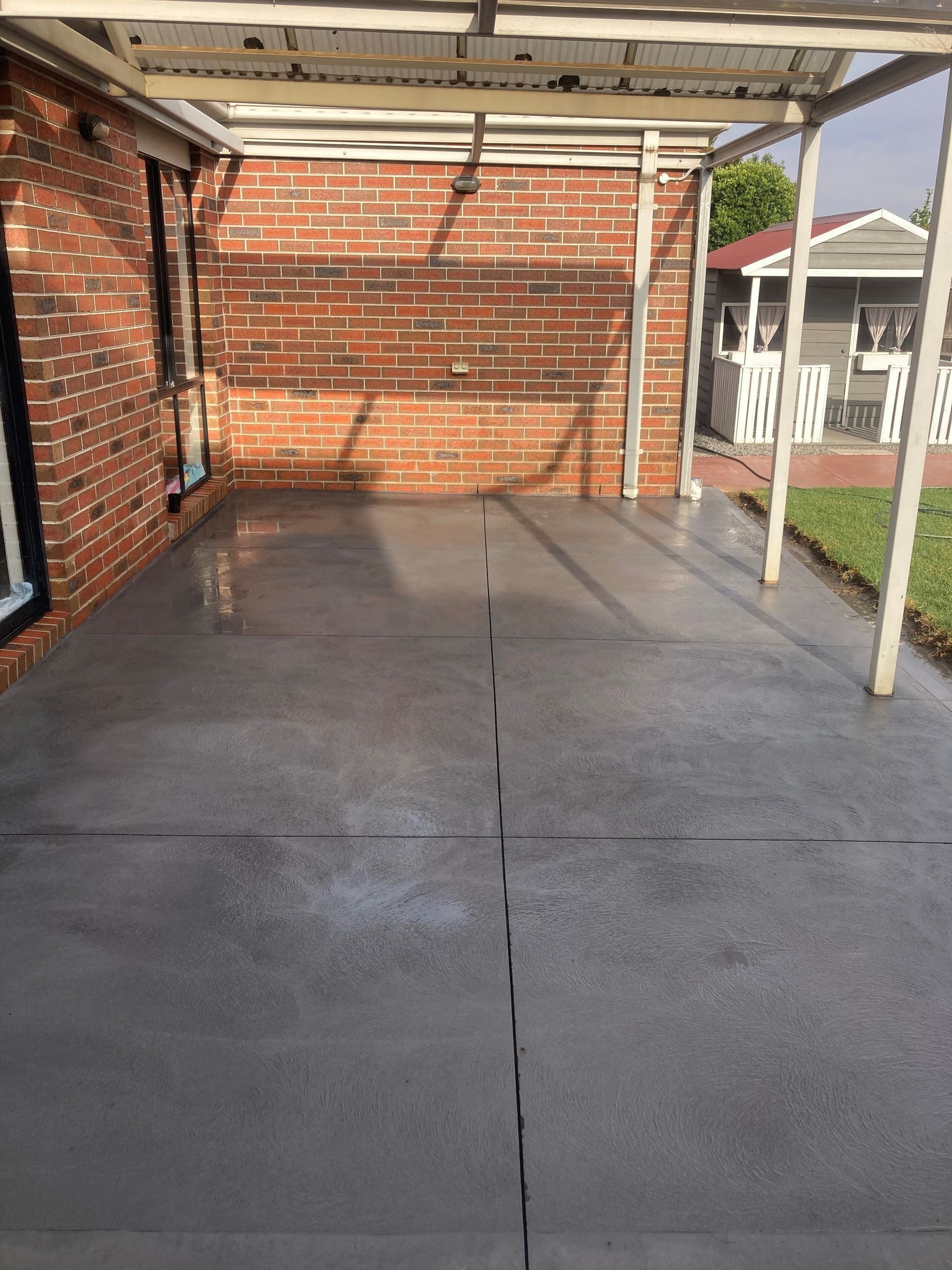 Gray concrete patio adjacent to a red brick wall, covered by a white metal awning.
