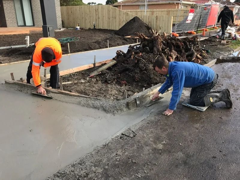 Two workers smoothing wet concrete on a sidewalk; construction site.