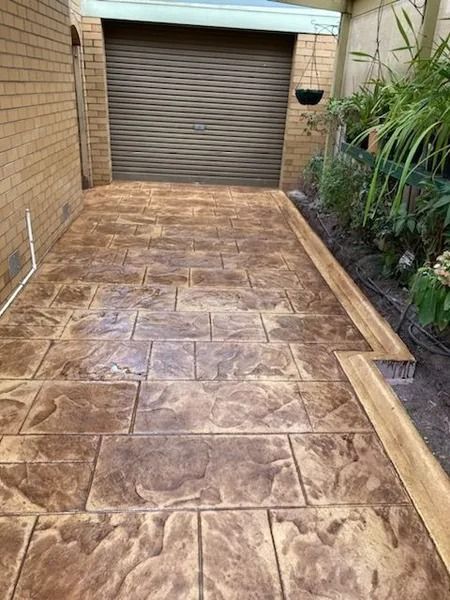 Stamped concrete driveway in brown tones, leading to a garage. Includes a wooden border and garden.