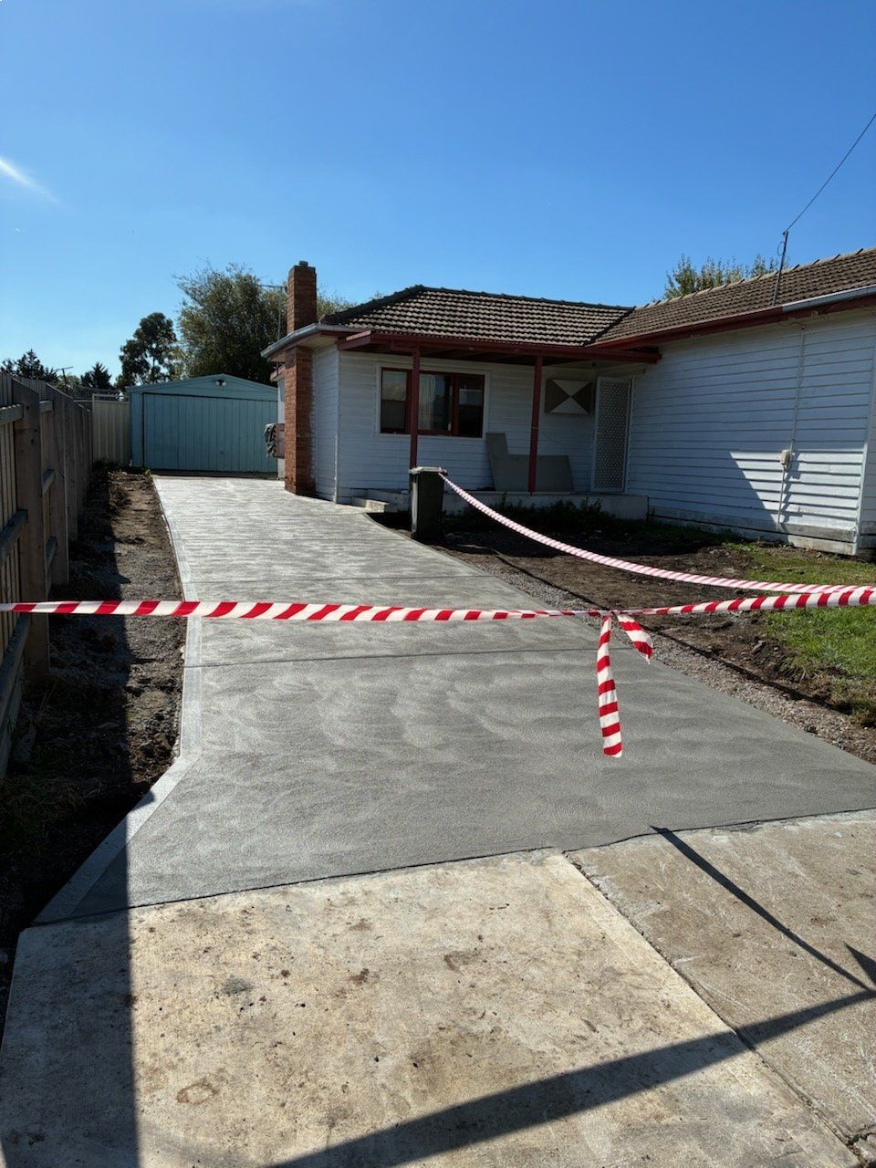 A newly paved driveway blocked by red and white caution tape in front of a house.