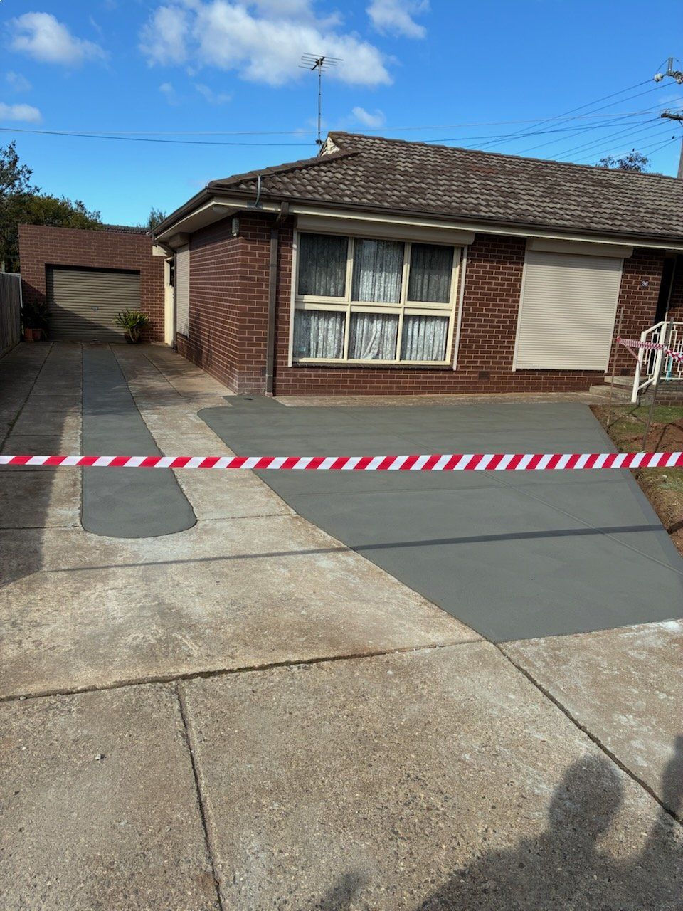 Driveway partially resurfaced with caution tape in front of a brick house.