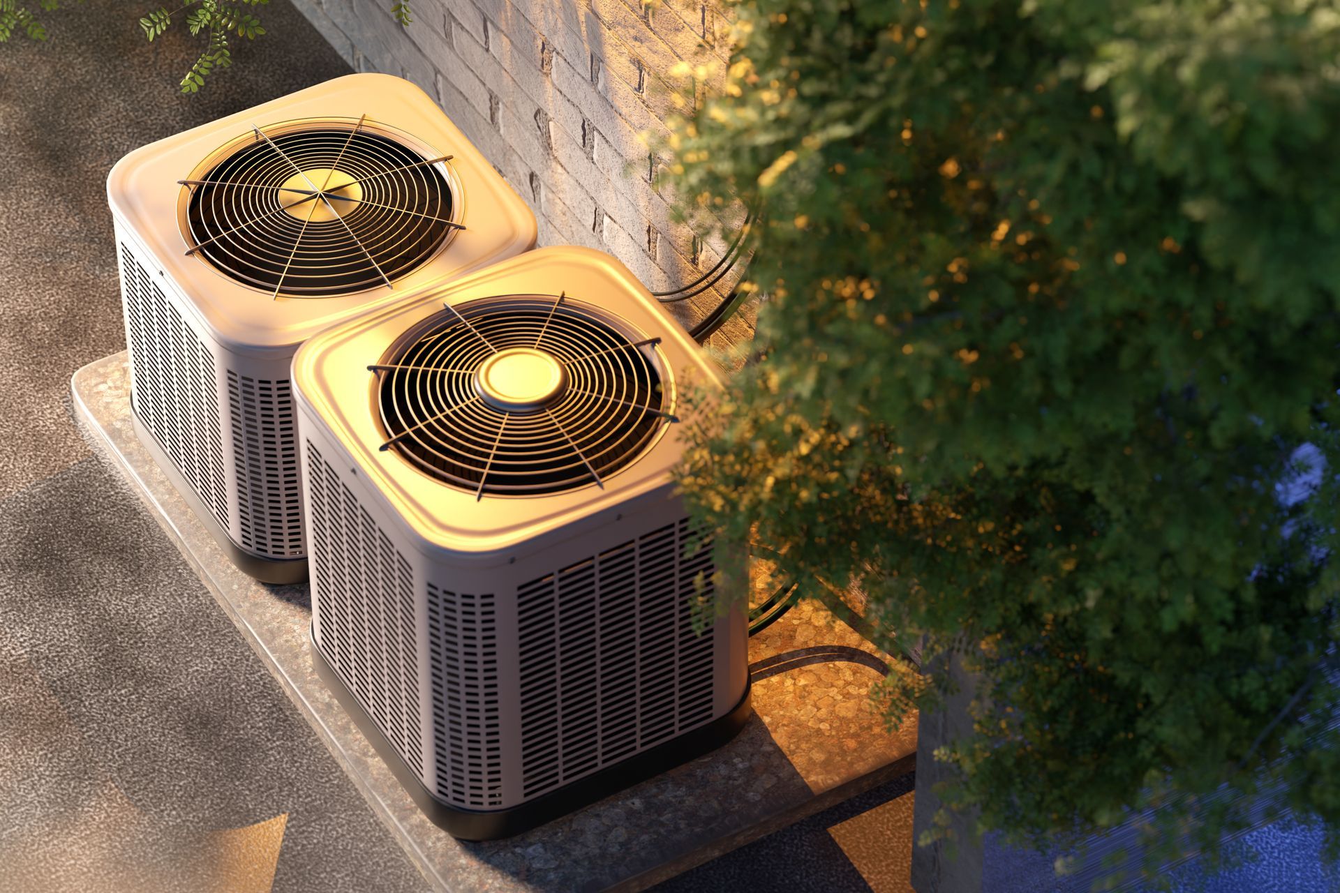 Two air conditioning units on a concrete pad next to a brick wall and green foliage.