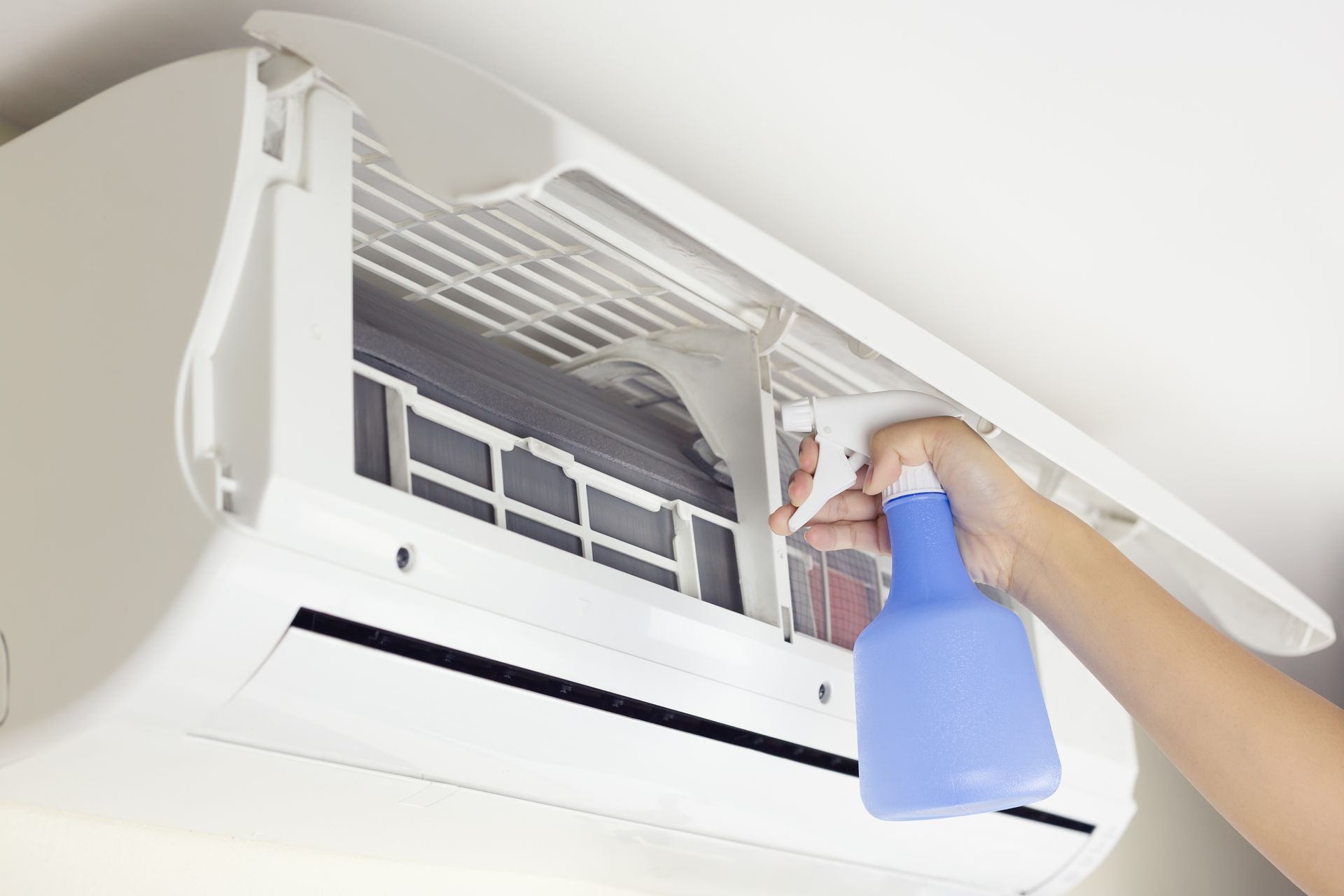Hand spraying cleaning solution into an open air conditioning unit's filter.