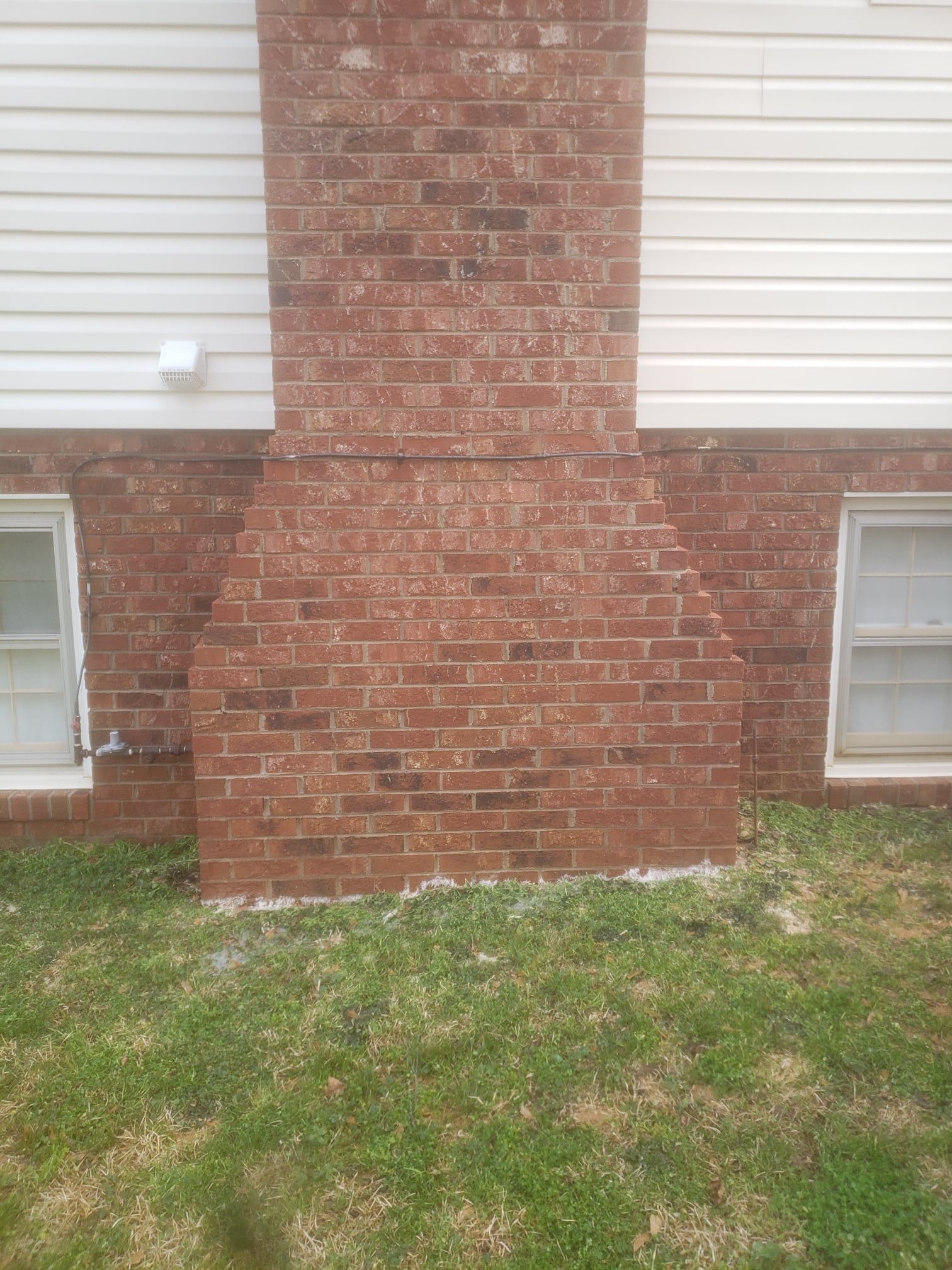 A red brick chimney on the side of a house with two windows.