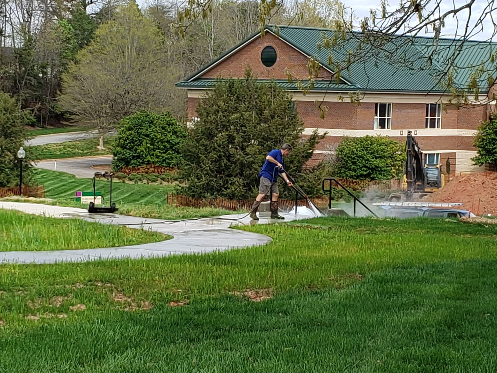 A man is using a pressure washer to clean a sidewalk in a park.