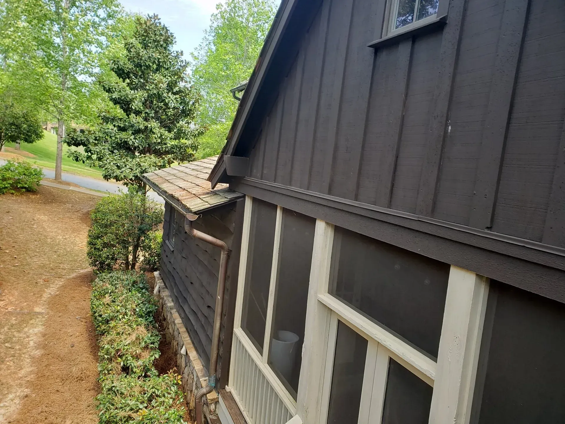 A black house with a screened in porch and trees in the background.