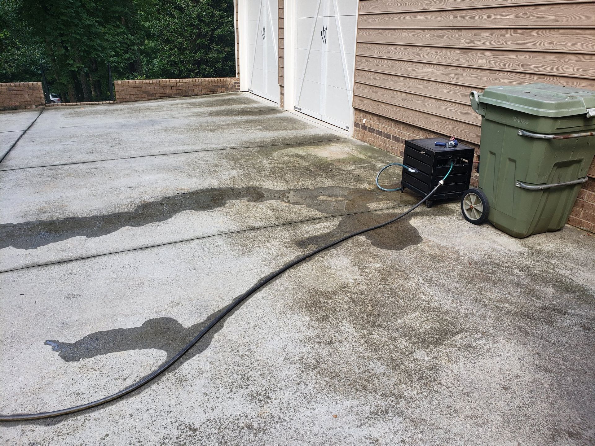 A green trash can is sitting on the side of a concrete driveway next to a generator.