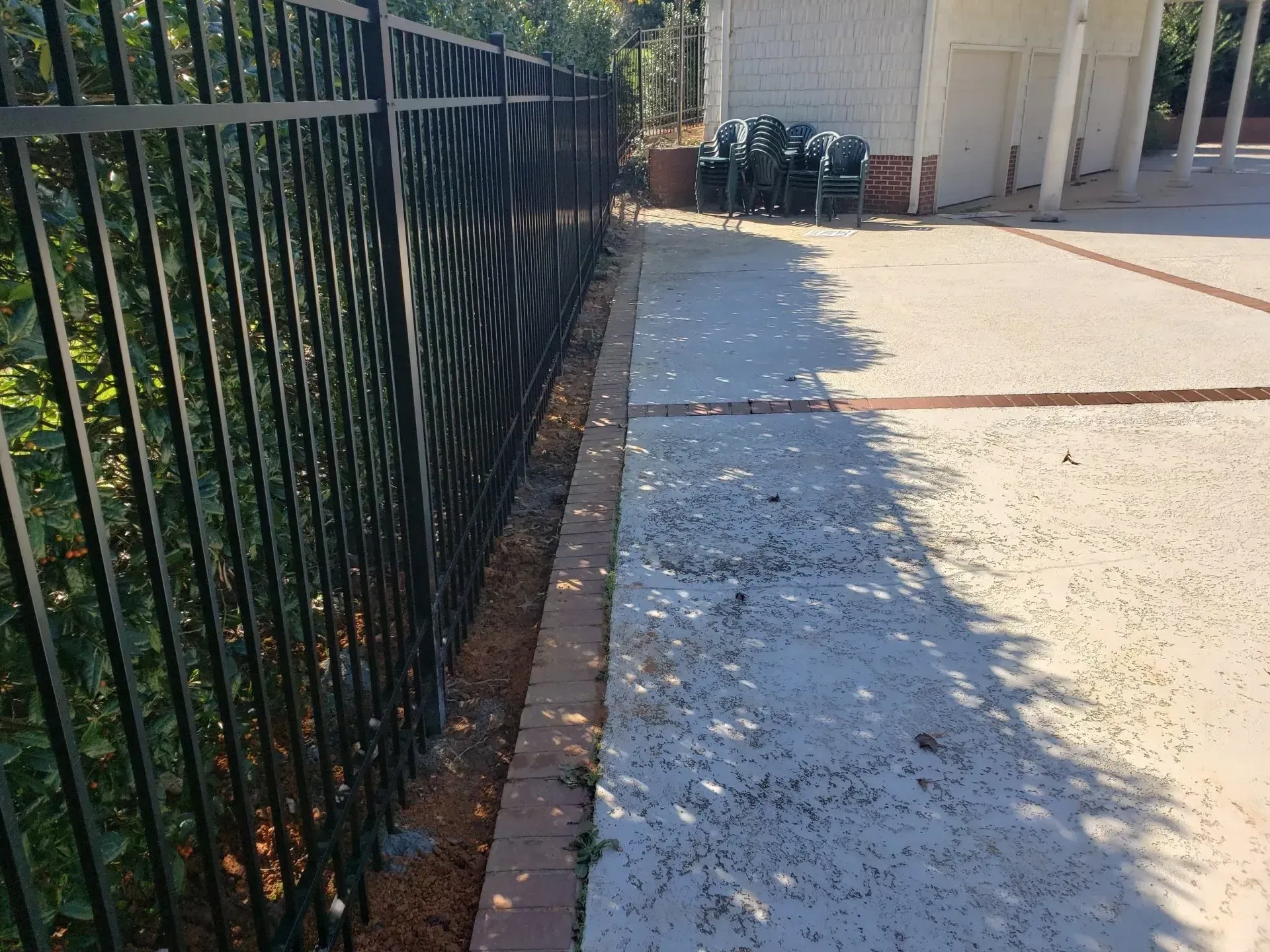 A black fence surrounds a concrete walkway next to a building.