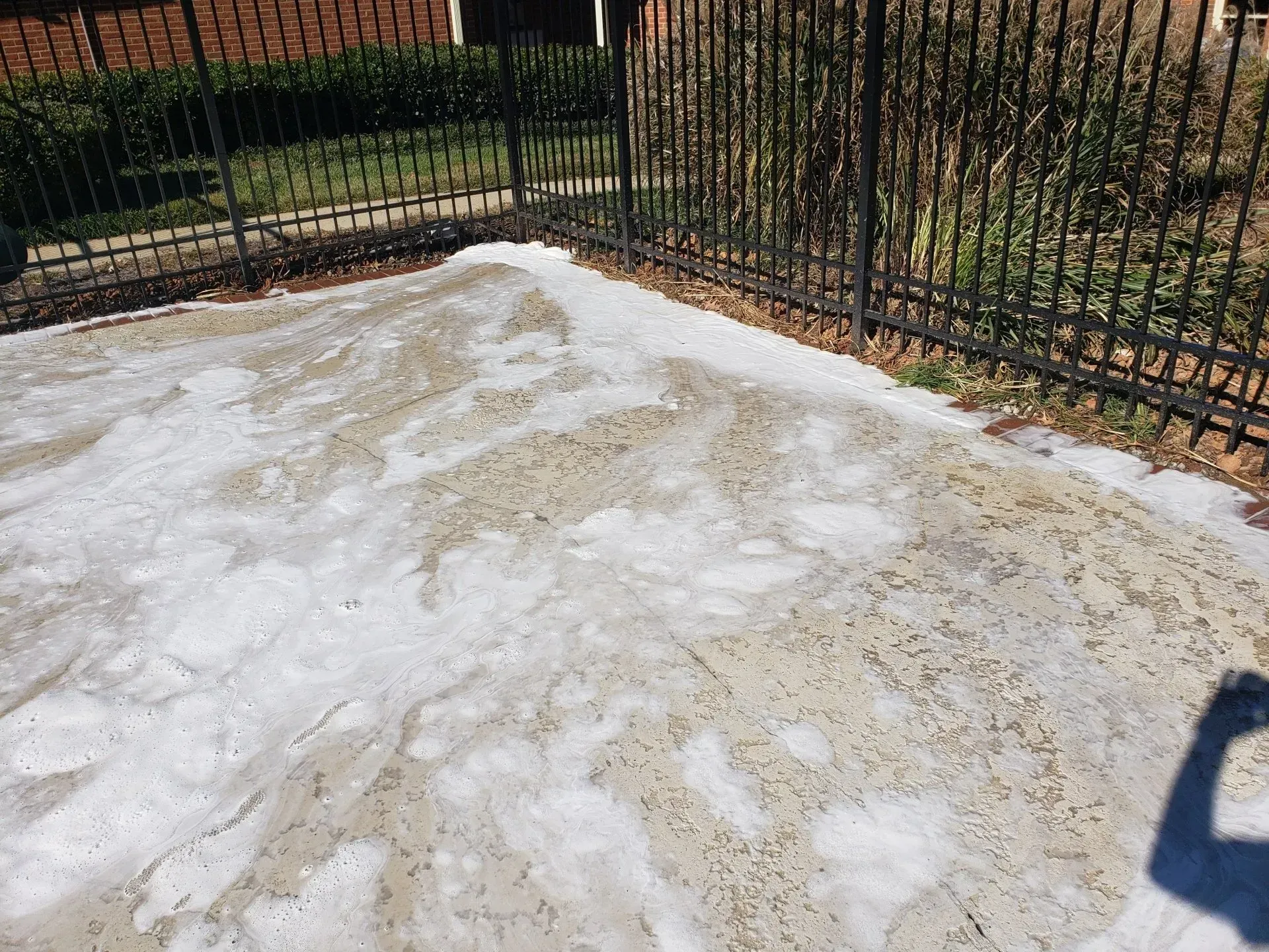 A concrete driveway with a wrought iron fence in the background.
