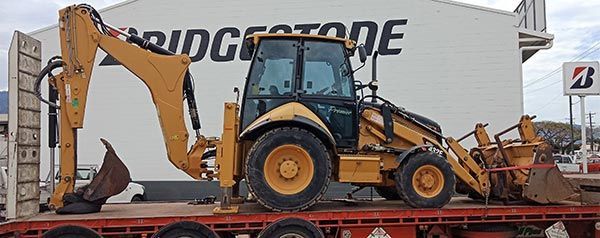 A bulldozer is sitting on top of a flatbed truck in front of a building.