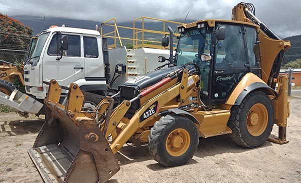 A bulldozer is parked next to a white truck in a dirt lot.