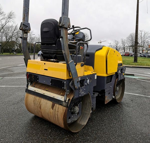 A yellow and black road roller is parked in a parking lot