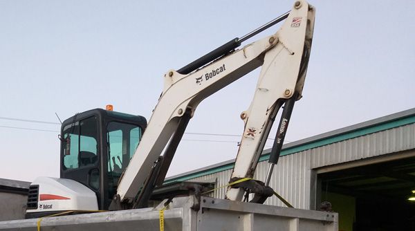 A bobcat excavator is sitting on top of a dumpster.