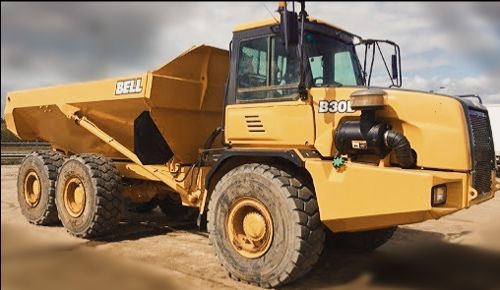 A yellow bell dump truck is parked in the dirt
