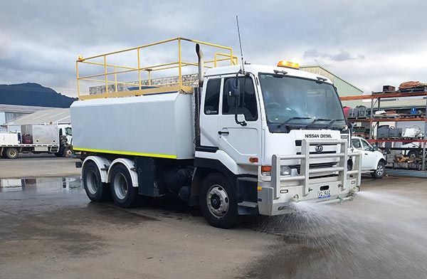A white truck is spraying water on the ground in a parking lot.