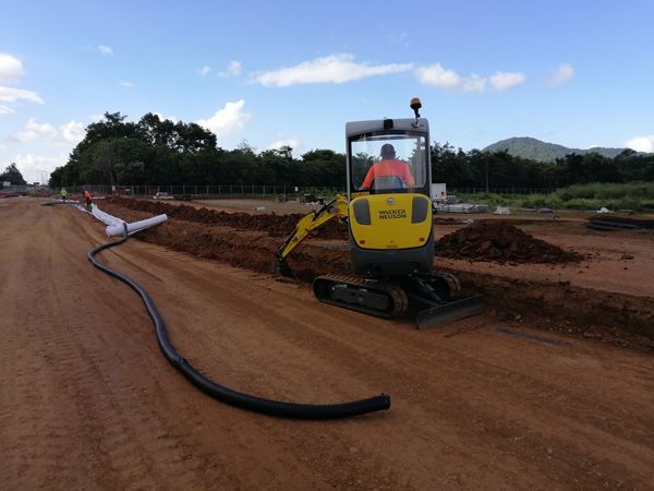 A man is driving a yellow excavator on a dirt road