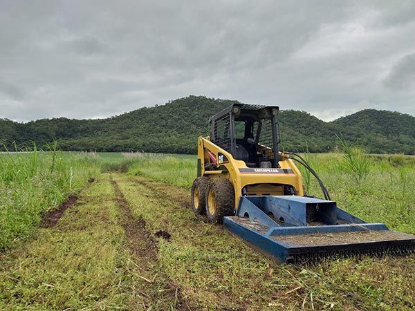 A yellow and blue tractor is cutting grass in a field.