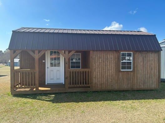 Brown cabin with porch, white door, and windows under a blue sky.