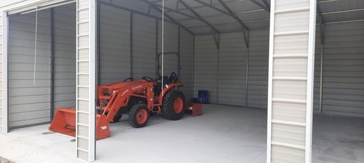 An orange tractor inside a metal shed.