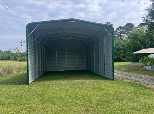 Green metal carport on a grassy area, open entrance, sunny day.