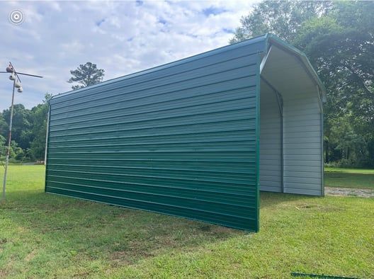Green metal carport on green grass, under a cloudy sky.