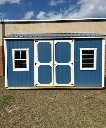 Blue shed with white trim, double doors, and windows, on brown grass.