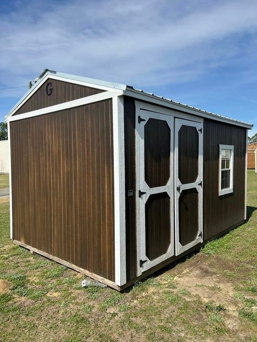 Brown shed with white trim, double doors, and a small window on a grassy lawn.