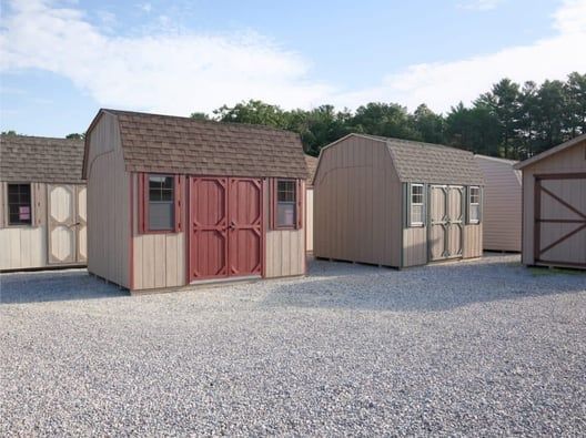Several beige storage sheds with brown roofs and doors on a gravel lot.