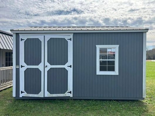 Gray shed with white trim, double doors, a window, and a metal roof against a cloudy sky.