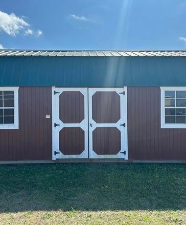 Red barn with white double doors and windows, blue roof, green trim, sunny day.