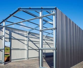 Steel-framed building under construction with corrugated metal siding against a clear blue sky.