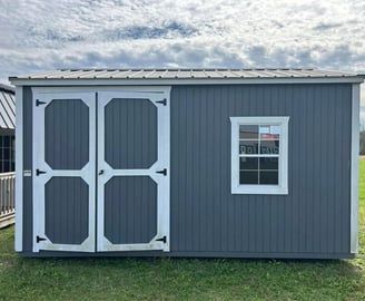 Gray shed with white-trimmed doors and window, metal roof, on green grass.