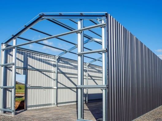Metal-framed shed under construction with corrugated steel walls, blue sky. Open doorway.