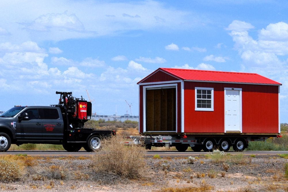 Truck towing a red shed with an open cargo door on a sunny road.